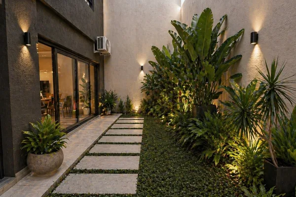 Render nocturno de un sendero lateral con pasos de piedra, follaje tropical y luz rasante sobre el muro